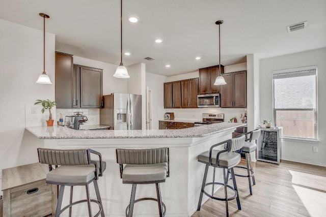 kitchen featuring a peninsula, light wood-type flooring, stainless steel appliances, and visible vents