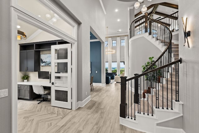 entryway with built in desk, a high ceiling, baseboards, light wood-style floors, and stairs