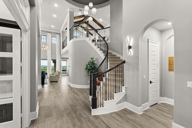 foyer with a towering ceiling, a notable chandelier, arched walkways, and wood finished floors