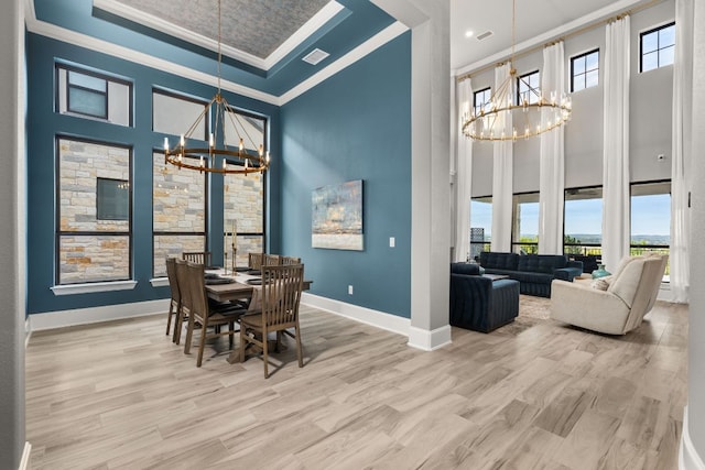 dining room featuring light wood finished floors, an inviting chandelier, crown molding, and a high ceiling