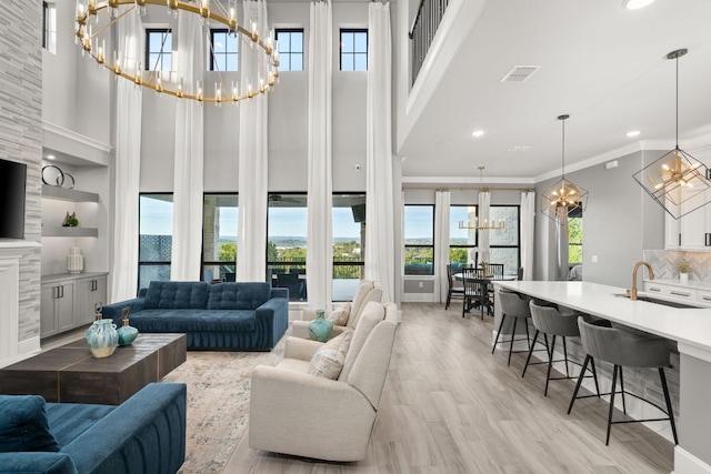 living room featuring an inviting chandelier, a high ceiling, light wood-type flooring, visible vents, and ornamental molding