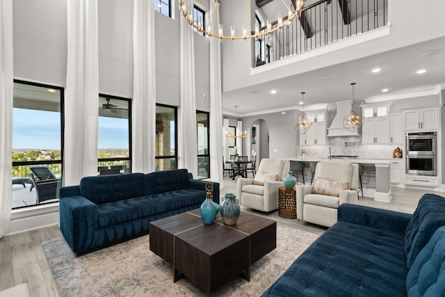 living room with an inviting chandelier, a towering ceiling, crown molding, and recessed lighting