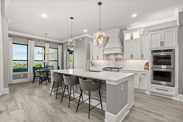 kitchen featuring a sink, a notable chandelier, double oven, premium range hood, and ornamental molding