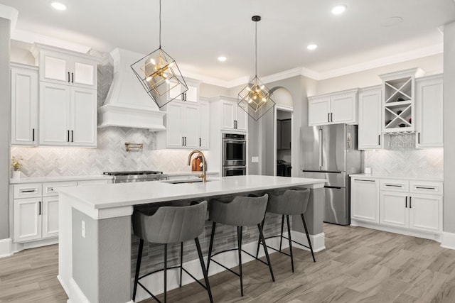 kitchen with a sink, premium range hood, white cabinetry, backsplash, and appliances with stainless steel finishes
