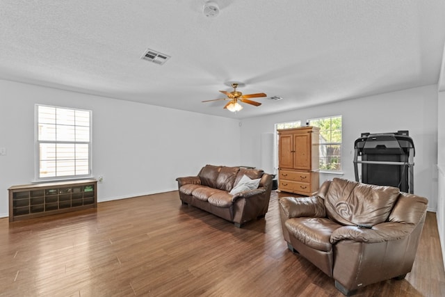 living room featuring wood finished floors, a textured ceiling, visible vents, a ceiling fan, and baseboards