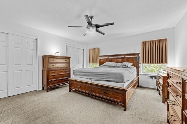 bedroom featuring light carpet, baseboards, a ceiling fan, and multiple closets