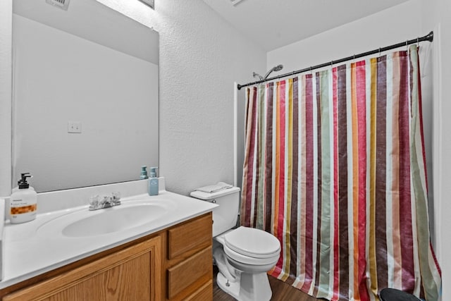 full bath featuring toilet, wood finished floors, a shower with shower curtain, a textured wall, and vanity