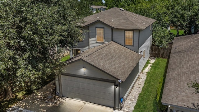 traditional home featuring concrete driveway, roof with shingles, an attached garage, and fence