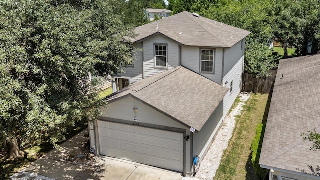 traditional-style home featuring concrete driveway, a garage, a shingled roof, and fence