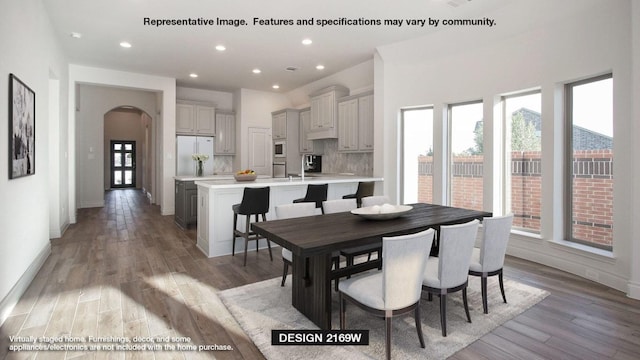 dining space featuring arched walkways, baseboards, light wood-style flooring, and recessed lighting