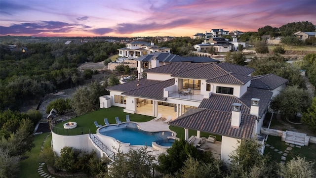5609 Laceback Ter, Austin, TX 78738 - back of property at dusk featuring a balcony, a pool with connected hot tub, a patio area, stucco siding, and a fenced backyard