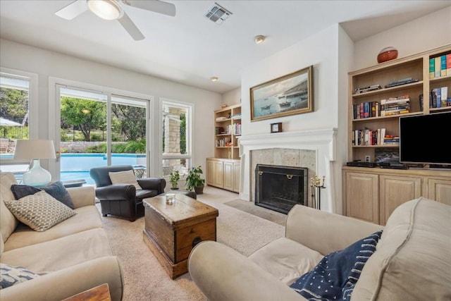 living room featuring a tile fireplace, visible vents, ceiling fan, and light carpet