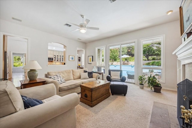 carpeted living room with a fireplace with flush hearth, baseboards, a ceiling fan, and visible vents