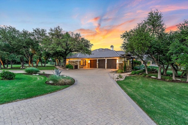 view of front of house with an attached garage, stone siding, a lawn, curved driveway, and a standing seam roof