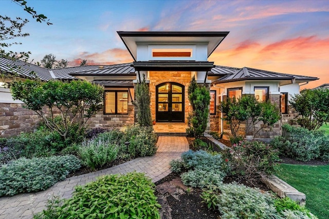 property entrance featuring metal roof, a standing seam roof, stone siding, and french doors
