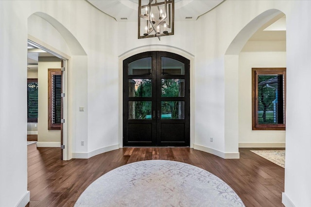 foyer featuring a notable chandelier, french doors, dark wood-type flooring, arched walkways, and a high ceiling