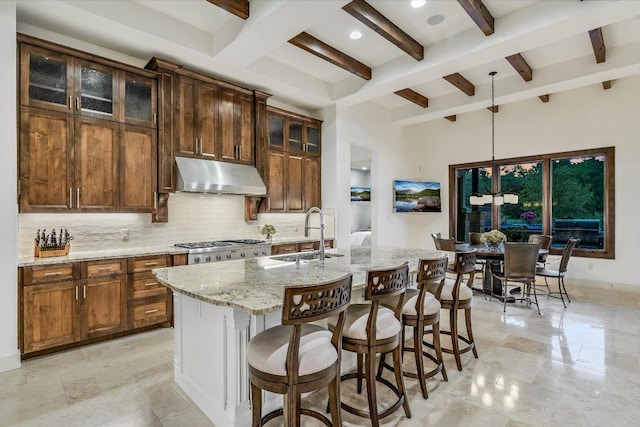 kitchen featuring under cabinet range hood, a sink, decorative backsplash, beamed ceiling, and light stone counters