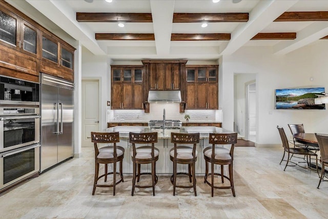 kitchen with stainless steel appliances, under cabinet range hood, beamed ceiling, coffered ceiling, and decorative backsplash