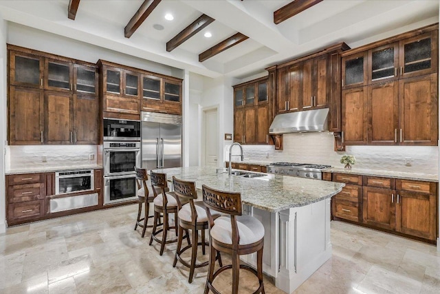 kitchen featuring a sink, under cabinet range hood, beamed ceiling, decorative backsplash, and a kitchen breakfast bar