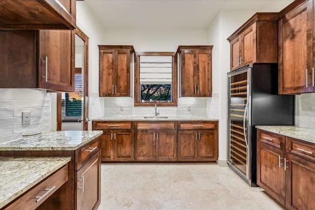 kitchen featuring backsplash, light stone counters, stainless steel refrigerator, and a sink