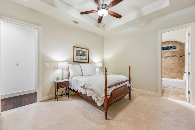 bedroom with carpet floors, baseboards, a tray ceiling, ensuite bathroom, and a ceiling fan