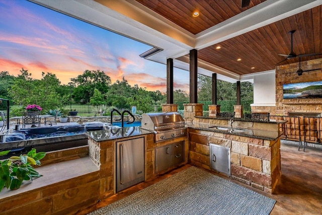 patio terrace at dusk with a sink, area for grilling, a grill, outdoor wet bar, and a ceiling fan