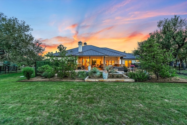 back of house at dusk with a yard, fence, a standing seam roof, and a chimney