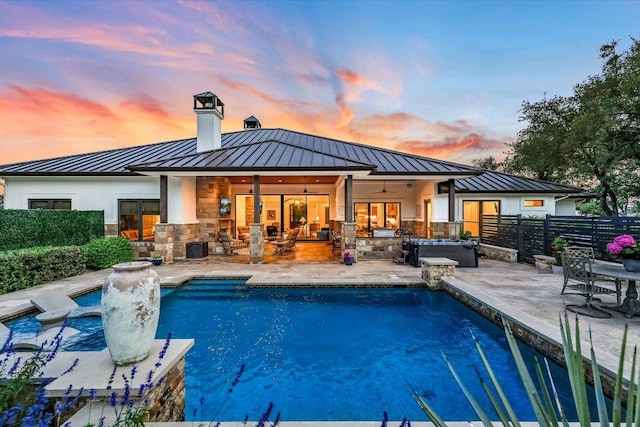 back of house at dusk with a standing seam roof, metal roof, a chimney, fence, and a patio