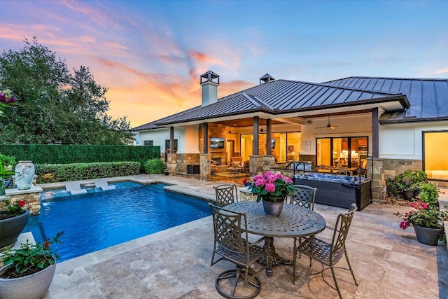 back of house featuring a standing seam roof, stone siding, metal roof, a patio, and a ceiling fan