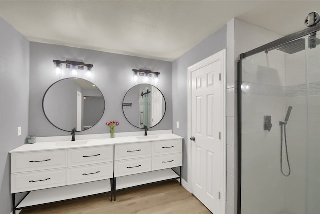 full bathroom featuring a sink, double vanity, a shower stall, and wood finished floors
