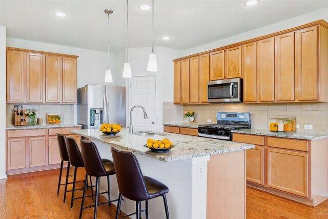 6900 Longford Trl, Austin, TX 78754 - kitchen featuring appliances with stainless steel finishes, light wood-style floors, light stone counters, a center island with sink, and recessed lighting
