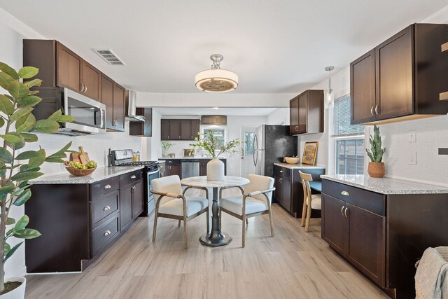 kitchen with appliances with stainless steel finishes, decorative backsplash, wall chimney exhaust hood, dark brown cabinets, and light wood-type flooring