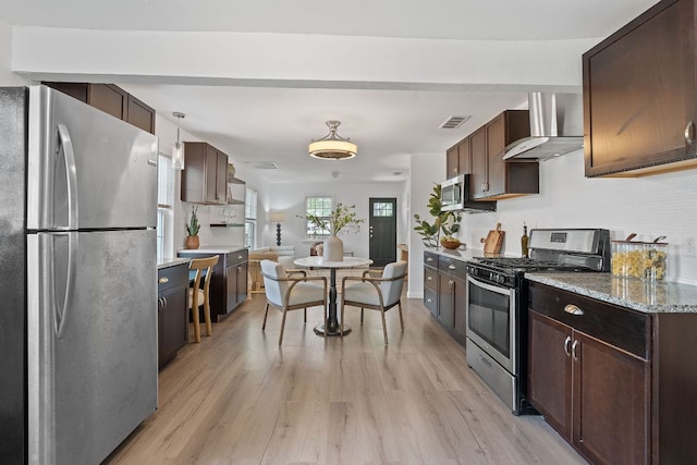 kitchen with stainless steel appliances, wall chimney range hood, light wood finished floors, and decorative backsplash