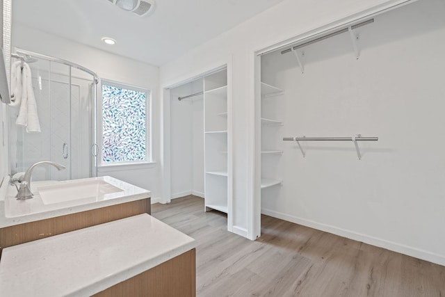 bathroom featuring a sink, wood finished floors, a shower stall, a walk in closet, and baseboards