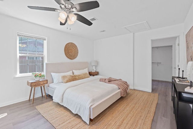 bedroom featuring attic access, wood finished floors, baseboards, a ceiling fan, and a walk in closet