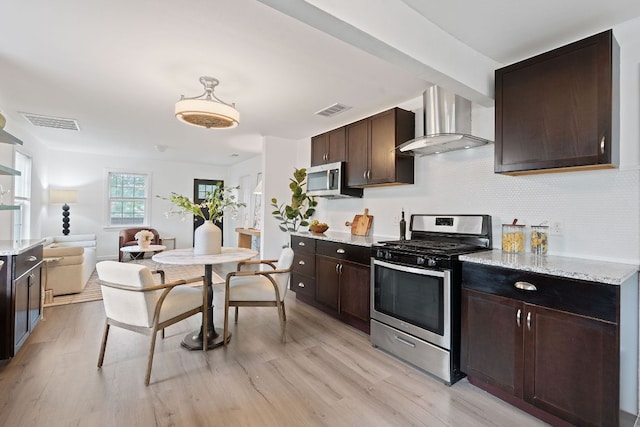 kitchen featuring appliances with stainless steel finishes, wall chimney exhaust hood, dark brown cabinetry, and light wood-style flooring