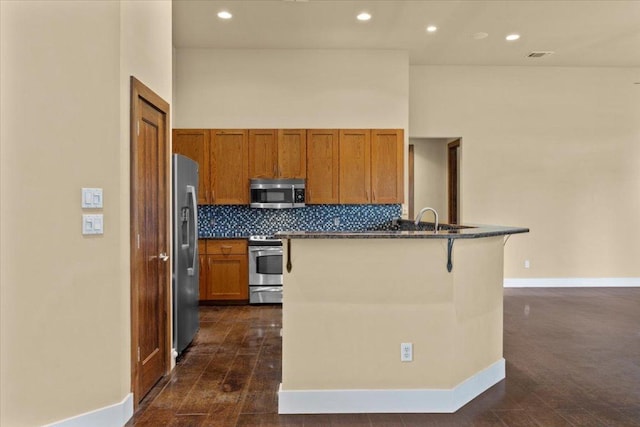 kitchen with stainless steel appliances, dark countertops, backsplash, a breakfast bar area, and baseboards