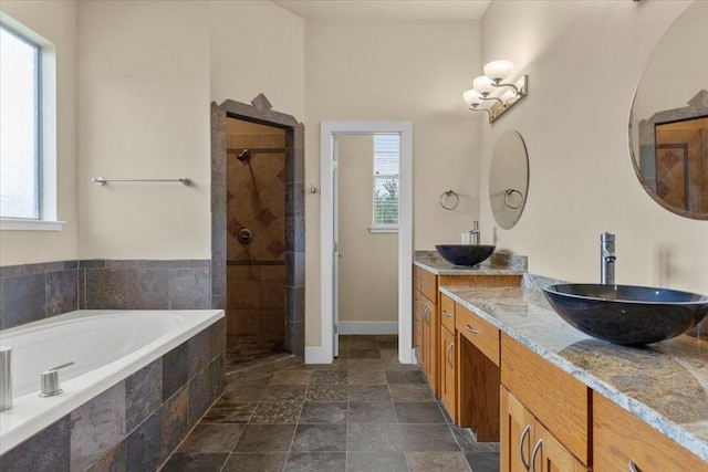 bathroom with stone finish floors, plenty of natural light, a stall shower, and double vanity