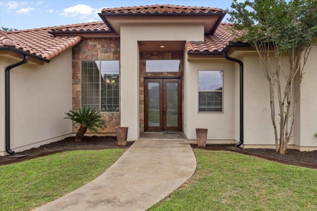 2450 Great Oaks Dr, San Marcos, TX 78666 - view of exterior entry featuring a tiled roof, french doors, stucco siding, and a lawn