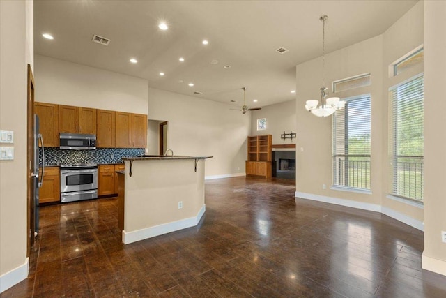 kitchen featuring appliances with stainless steel finishes, brown cabinets, open floor plan, dark countertops, and a chandelier