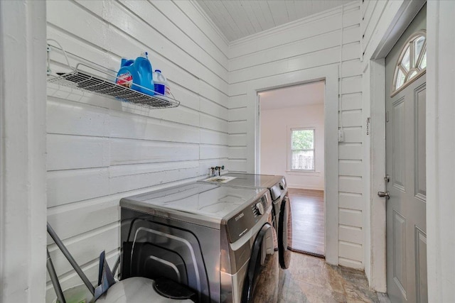 clothes washing area with washing machine and dryer, wooden walls, stone finish flooring, and crown molding