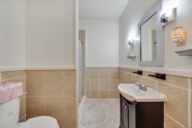bathroom with tile walls, toilet, a shower with curtain, vanity, and wainscoting