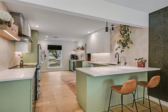 6802 Rio Bravo Ln, Austin, TX 78737 - kitchen with green cabinets, wall chimney exhaust hood, light wood-style flooring, a kitchen bar, and recessed lighting