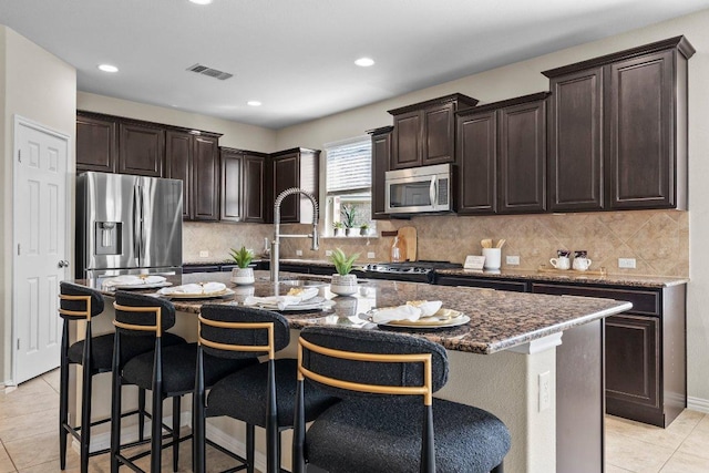 2020 Elaina Loop, Leander, TX 78641 - kitchen with appliances with stainless steel finishes, a breakfast bar area, dark stone countertops, light tile patterned flooring, and a kitchen island with sink