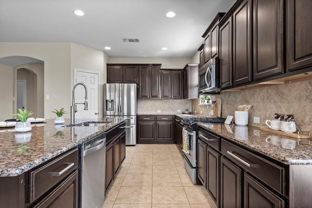 2020 Elaina Loop, Leander, TX 78641 - kitchen featuring stainless steel appliances, a sink, arched walkways, dark brown cabinetry, and backsplash