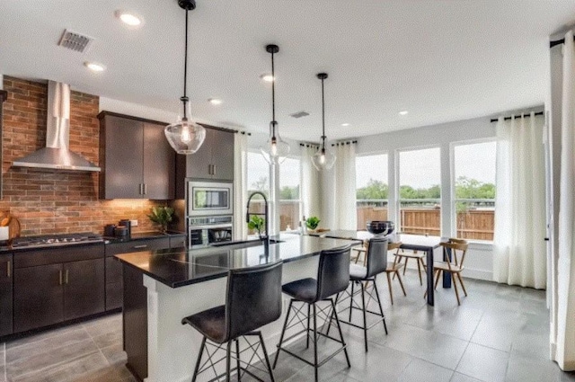 kitchen featuring wall chimney range hood, dark countertops, a breakfast bar, stainless steel appliances, and a sink