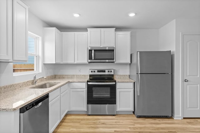 kitchen with stainless steel appliances, a sink, white cabinets, light stone countertops, and light wood-style flooring
