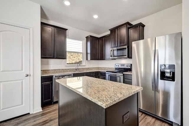 1174 Amy Dr, Kyle, TX 78640 - kitchen with stainless steel appliances, dark brown cabinetry, a center island, wood finished floors, and light stone countertops