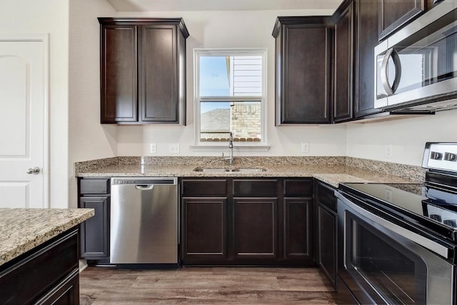 1174 Amy Dr, Kyle, TX 78640 - kitchen with appliances with stainless steel finishes, a sink, light stone counters, light wood finished floors, and dark brown cabinetry