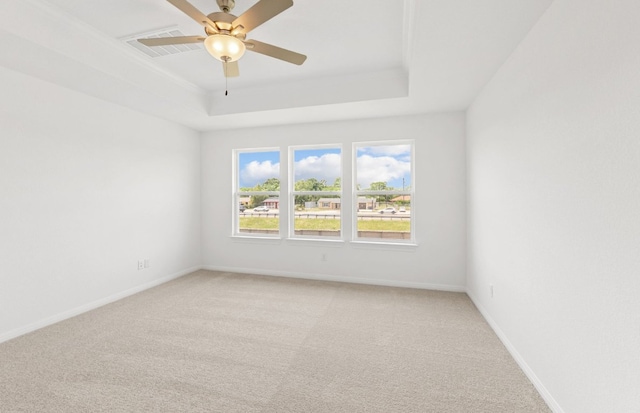 empty room with a raised ceiling, light carpet, ceiling fan, and baseboards